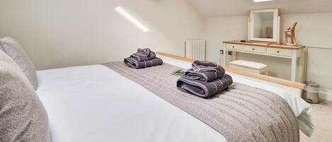 A bedroom with a bed, two rolled towels, a bedside table, a mirror, and a skylight.