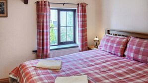 Un dormitorio con cama, ventana con cortinas, mesita de noche con lámpara y radiador.