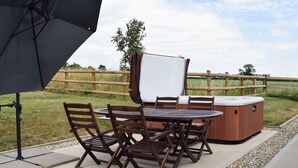 Een terras met een jacuzzi, houten tafel en stoelen.