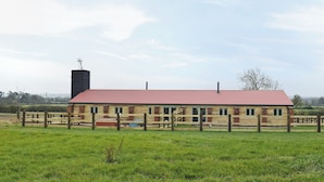 Een houten gebouw met een rood dak, omgeven door een houten hek, gelegen in een grasveld.