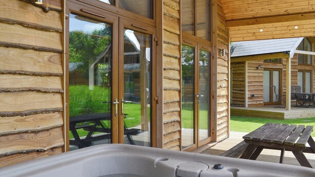 A wooden cabin with a hot tub, glass doors, and a patio with a table and chairs. - 2 bedroom accommodation in Thorpe on the Hill, near Lincoln (Thorpe on the Hill, near Lincoln)