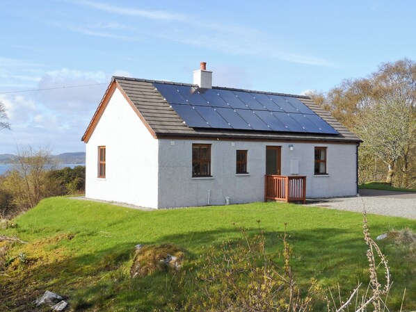 A single-story house with a sloped roof, a small porch, and solar panels on the roof.