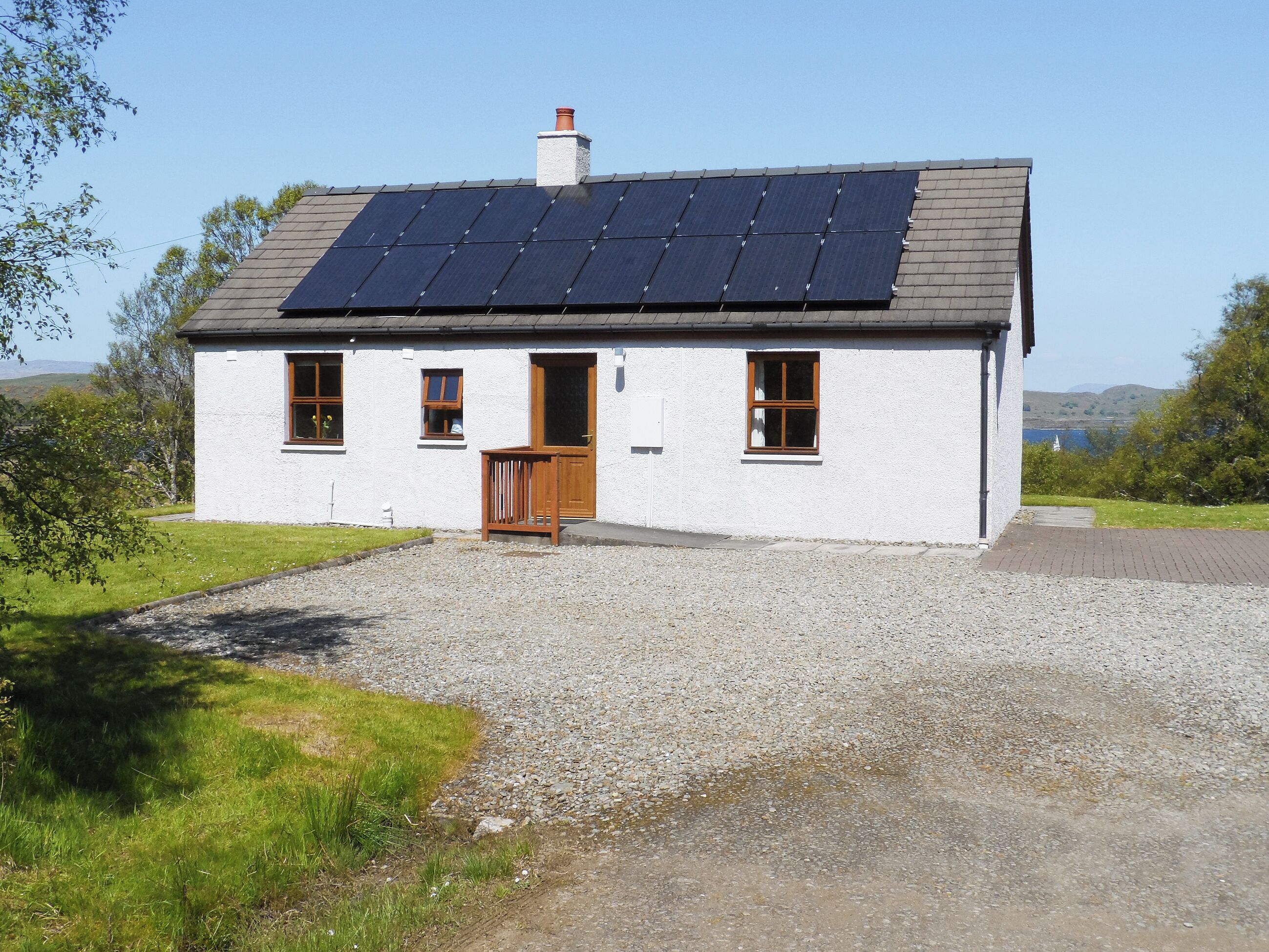 A white house with a gravel driveway, a wooden door, and solar panels on the roof.