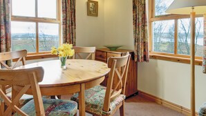 Un comedor con una mesa redonda de madera, sillas con estampado floral y un jarrón con flores amarillas.