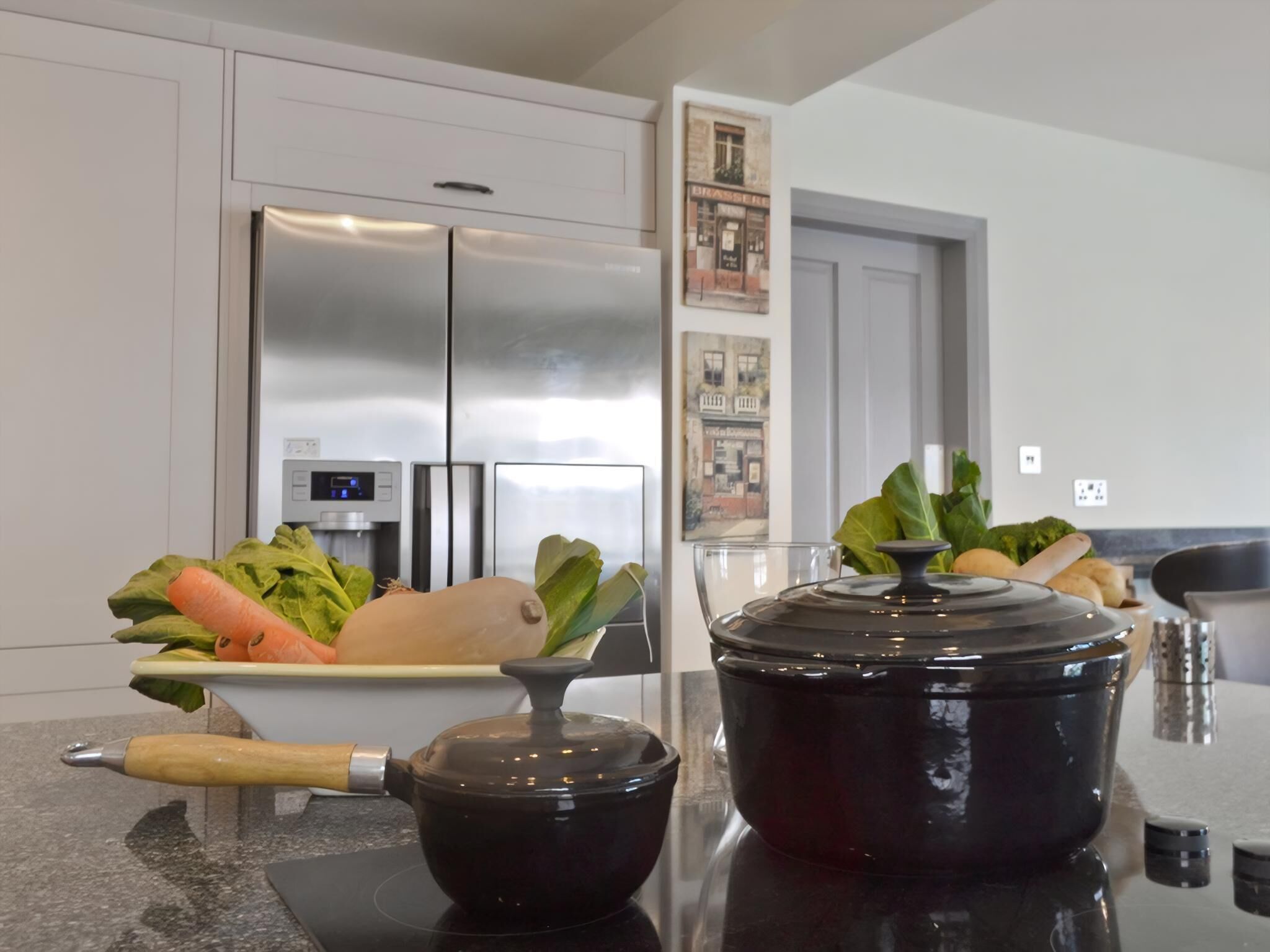 A kitchen with a stainless steel refrigerator, a stove with a pot, and a bowl of vegetables on the counter.