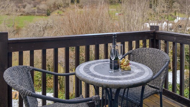 A deck with wicker chairs and a table, a bottle of champagne, and two glasses. - 4 bedroom accommodation in Trusham, near Newton Abbot (Trusham, near Newton Abbot)