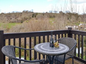 A deck with wicker chairs and a table, a bottle of champagne, and two glasses.