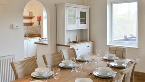 A dining room with a wooden table set for six, white chairs, a white cabinet, and a window with a view. - 4 bedroom accommodation in Trusham, near Newton Abbot (Trusham, near Newton Abbot)