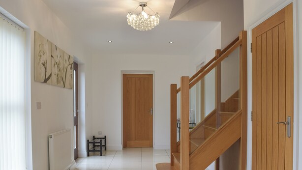 A hallway with a wooden staircase, a radiator, a small table, and a door. - 6 bedroom accommodation in Stepaside, near Saundersfoot (Stepaside, near Saundersfoot)