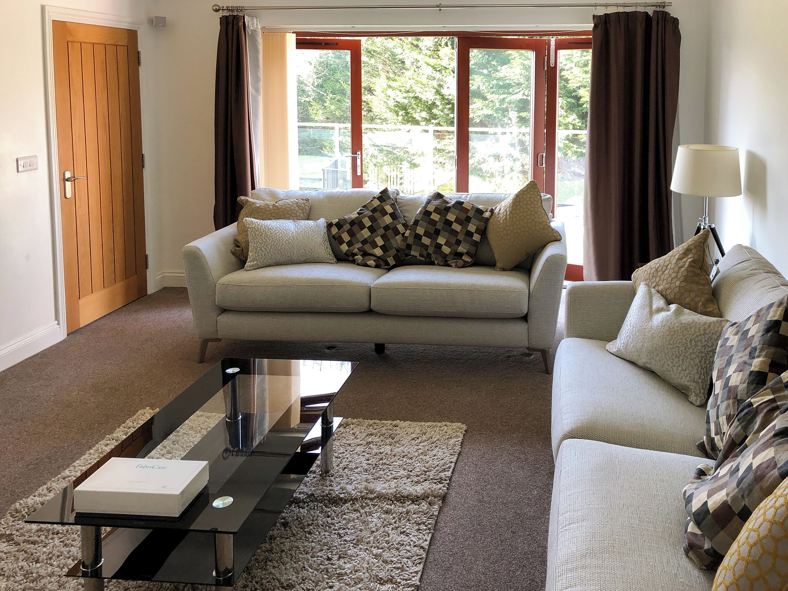 A living room with a sofa, a coffee table, and a lamp. There is a door and a window with curtains.