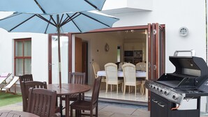 An outdoor patio with a round table, chairs, a grill, and a blue umbrella. - 6 bedroom accommodation in Stepaside, near Saundersfoot (Stepaside, near Saundersfoot)