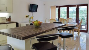 A modern kitchen with a wooden island, a dining area with chairs, a TV mounted on the wall, and a view through the glass door. - 6 bedroom accommodation in Stepaside, near Saundersfoot (Stepaside, near Saundersfoot)