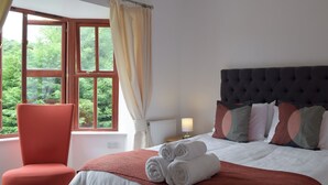 A bedroom with a bed, a chair, a window with curtains, and a view of greenery outside. - 6 bedroom accommodation in Stepaside, near Saundersfoot (Stepaside, near Saundersfoot)