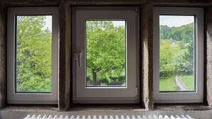 Una stanza con tre finestre che danno su un paesaggio verde.