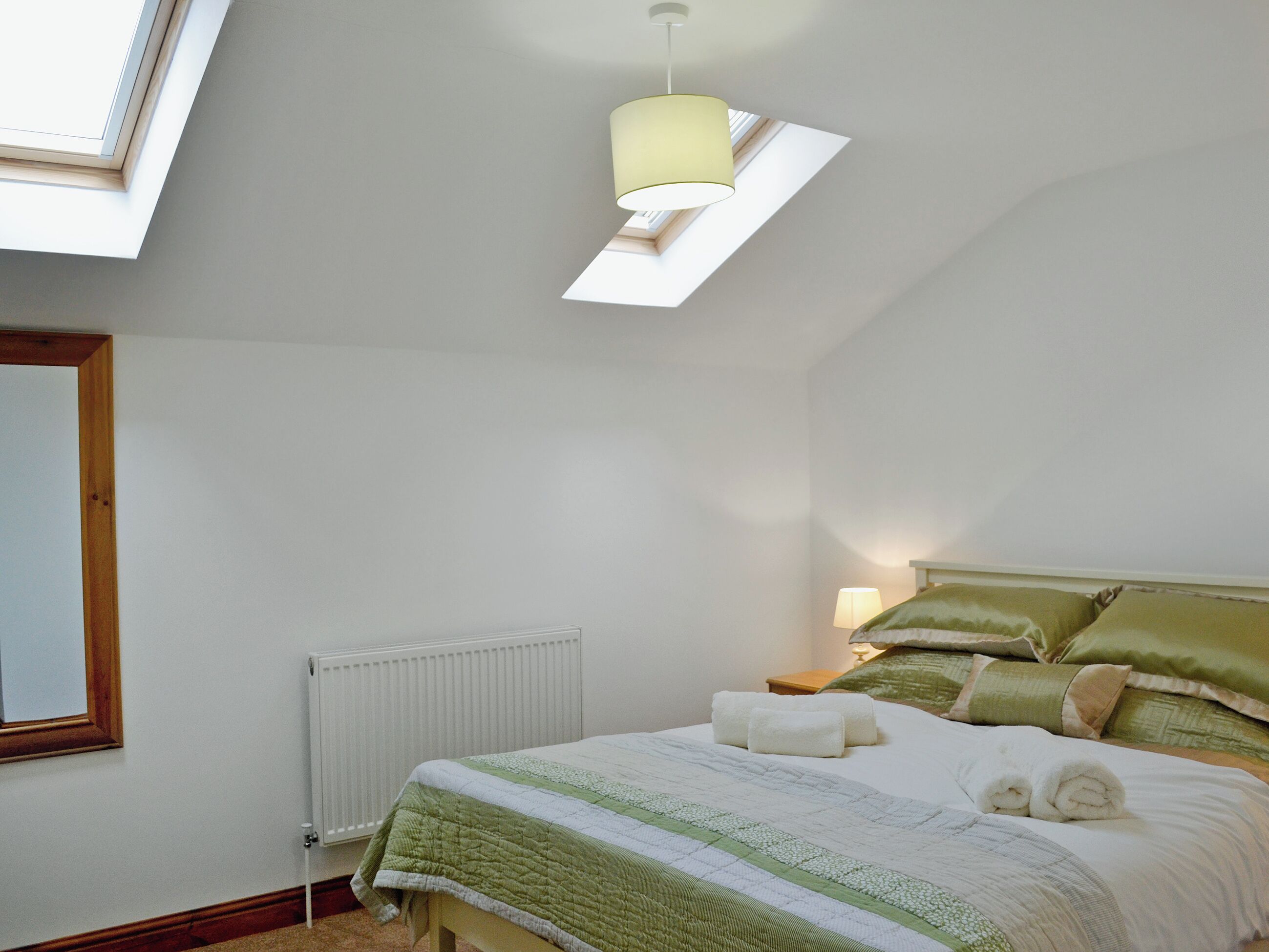 A bedroom with a skylight, a radiator, a bed with green bedding, and a bedside lamp.