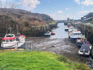 Um porto com barcos atracados ao longo de um canal estreito, cercado por margens gramadas e terreno rochoso.