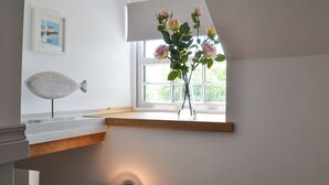 Et værelse med en træhylde, en vase med blomster, en vægmonteret lampe og et indrammet billede.
