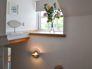A room with a wooden shelf, a vase with flowers, a wall-mounted light, and a framed picture.