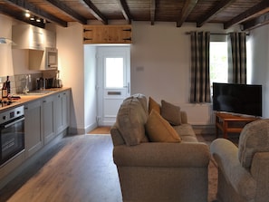 Una cocina moderna con electrodomésticos integrados, una zona de comedor con sofá y cojines, y un televisor en la sala.