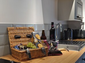 Una encimera de cocina con una cesta de mimbre que contiene aperitivos, una botella de vino tinto y una bolsa de patatas fritas.