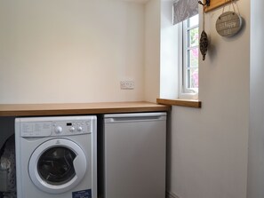 A laundry area with a front-loading washing machine and a dryer, a wooden countertop, a window with a view of pink flowers, and a wall-mounted sign that reads "THIS IS OUR HAPPY PLACE".