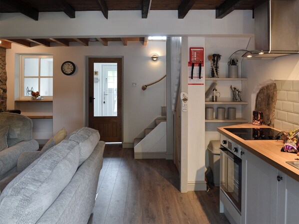 Una cocina moderna con encimera de madera, horno empotrado y campana extractora de acero inoxidable. Una escalera conduce a un segundo piso con una puerta y un reloj de pared.