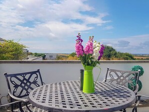 A round metal table with a green vase of flowers, two chairs, and a view of the countryside. - 2 bedroom accommodation in St Merryn, near Padstow (St Merryn, near Padstow)