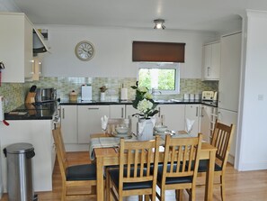 A kitchen with a dining table set for four, wooden chairs, a trash bin, and a clock on the wall. - 2 bedroom accommodation in St Merryn, near Padstow (St Merryn, near Padstow)