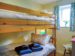 A bunk bed with a wooden frame, a bedside table with a lamp, and a window with curtains.