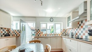 Una cocina con armarios blancos, salpicadero de azulejos, una mesa de comedor con mantel de lunares y un reloj en la pared.