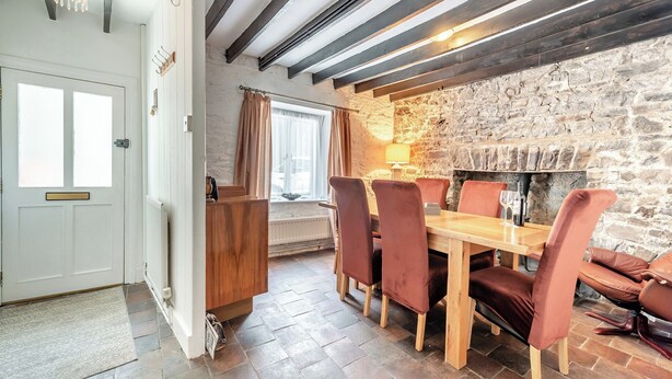 Comedor con pared de piedra, vigas de madera en el techo y una mesa dispuesta para cuatro.