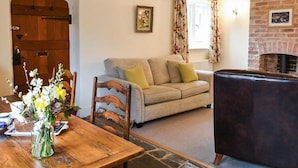 A cozy living room with a wooden dining table, a sofa, and a fireplace. - Enchanting 17th Century Cotswold Cottage in the beautiful village of Bretforton  (Bretforton, Evesham)