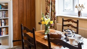 A wooden dining table with chairs, a vase of flowers, a teapot, and a tray with a loaf of bread and cups. - Enchanting 17th Century Cotswold Cottage in the beautiful village of Bretforton  (Bretforton, Evesham)