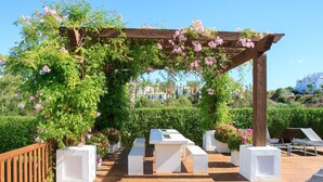 A wooden pergola with pink flowers, white planters, and a wooden deck. - Golf Hills Marbella - Beautiful decorated incl. lounge terrace (Estepona)