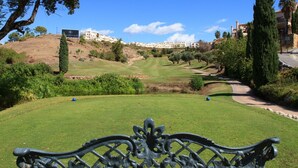 A golf course with a bench in the foreground, a sign for the El Corte Golf Club, and buildings in the background. - Golf Hills Marbella - Beautiful decorated incl. lounge terrace (Estepona)
