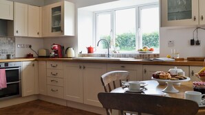 A modern kitchen with white cabinets, a large window, and a dining area with a wooden table and chairs. - 2 bedroom accommodation in Dwyran, near Llanfairpwllgwyngyll (Dwyran, near Llanfairpwllgwyngyll)
