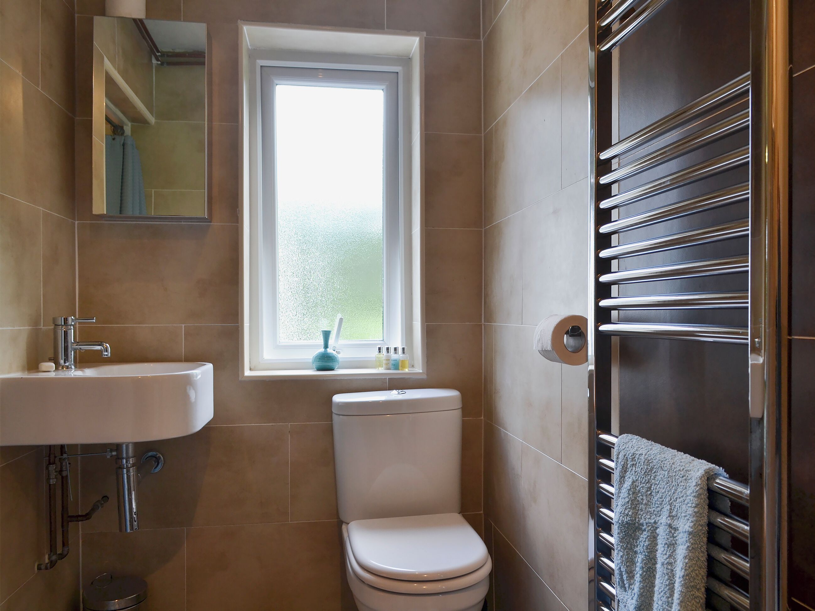 Une salle de bain avec un lavabo blanc, des toilettes, une fenêtre et un porte-serviettes.