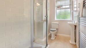 Ein Badezimmer mit Duschkabine aus Glas, Toilette, Waschbecken und einem Fenster mit Jalousien.