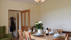 A dining area with a wooden table set for four, surrounded by wooden chairs with cushions. There is a potted plant on the table, and a bottle of wine is visible. - 3 bedroom accommodation in near Chipping Warden (near Chipping Warden)