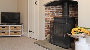 A room with a brick fireplace, a television on a white stand, and wicker baskets. - A great base for seaside enthusiasts. (Deal)