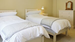 A bedroom with two single beds, a bedside table with a lamp, a dresser, and a mirror. - A great base for seaside enthusiasts. (Deal)