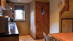 A kitchen with a wooden door, a window, and a dining area with a table and chairs. - 2 bedroom accommodation in Bussage, near Cirencester (Bussage, near Cirencester)