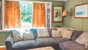 A cozy living room with a sectional sofa, a wooden coffee table, a bookshelf, a mirror, and a window with curtains. - 3 bedroom accommodation in Llanddona, near Beaumaris (Llanddona, near Beaumaris)