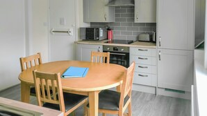 A compact kitchen with a round wooden table, four chairs, a microwave, a toaster, and a refrigerator. - 3 bedroom accommodation in Llanddona, near Beaumaris (Llanddona, near Beaumaris)