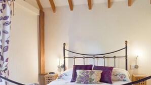 A neatly made bed with a floral bedspread, a headboard with a clock, and a wooden headboard on the left. - 2 bedroom accommodation in Upper Welland, near Malvern (Upper Welland, near Malvern)