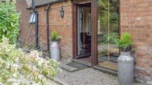 A brick building with a glass door entrance, a small garden area with potted plants, and a gravel pathway. - 2 bedroom accommodation in Upper Welland, near Malvern (Upper Welland, near Malvern)
