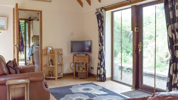 A living room with a sofa, a television, a wooden cabinet, and a large window with curtains. - 2 bedroom accommodation in Upper Welland, near Malvern (Upper Welland, near Malvern)