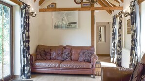 A cozy living room with a brown leather sofa, a wooden ceiling, and a sailboat painting on the wall. - 2 bedroom accommodation in Upper Welland, near Malvern (Upper Welland, near Malvern)
