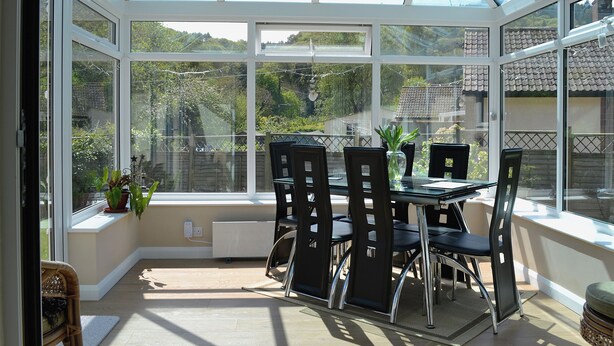 A conservatory with a glass roof, a table with chairs, and a view of the garden outside. - 4 bedroom accommodation in Dunster, near Minehead (Dunster, near Minehead)