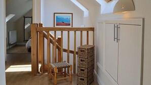 A room with a wooden staircase, a small wooden stool, a wicker basket, and a white cabinet. - 4 bedroom accommodation in Dunster, near Minehead (Dunster, near Minehead)